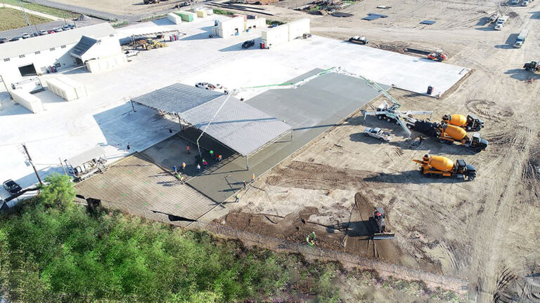 Concrete paving in progress at the Alpine Site Services site in Edna, TX, with mixer trucks and crew on site, by Keeton Construction Services