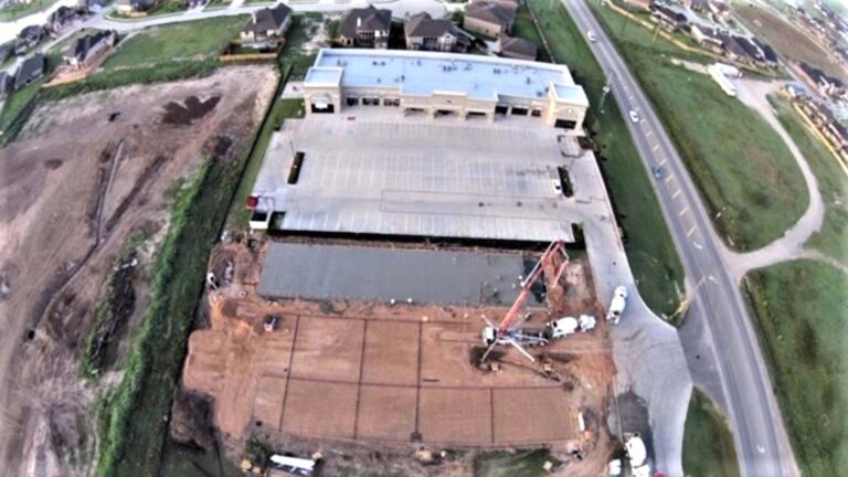 Aerial view of Cardiff Retail Center in Katy, TX during construction, showing the building, parking lot, and active concrete work with equipment on site -- Keeton Construction Services
