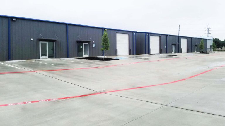 Ground-level view of a metal building facade with overhead doors and paved drive at Legacy Business Park in Cypress TX by Keeton Construction Services