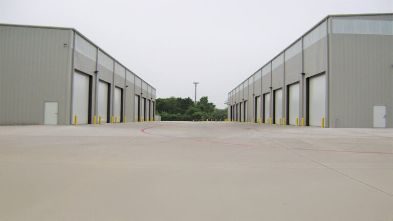 View between two facing rows of metal buildings at Master Rig International in Houston, TX by Keeton Construction Services showing paved drive and overhead doors