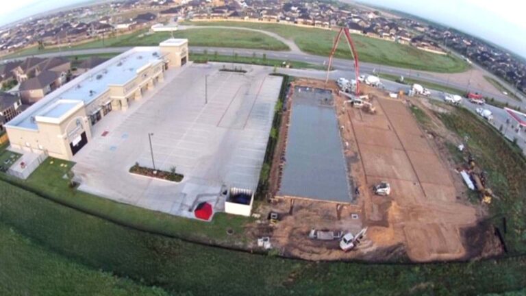 Aerial view of Cardiff Retail Center site in Katy, TX during construction, showing a standing building, parking lot, and concrete pour in progress -- Keeton Construction Services