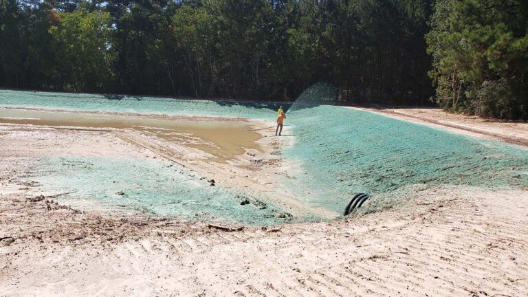 Site work at United Laser Cladding in Cypress, TX by Keeton Construction Services, with a worker applying erosion-control material to a bare-earth detention area