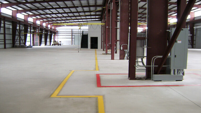 Interior of a large open bay at Master Rig International in Houston, TX by Keeton Construction Services with structural columns, an overhead crane rail, and floor markings