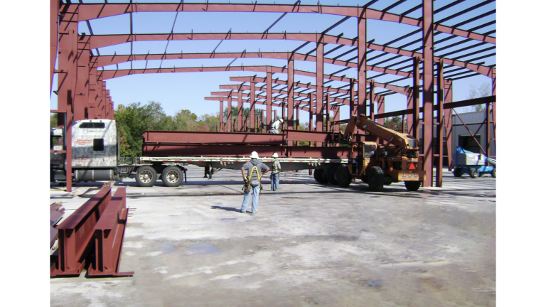 Structural steel framing during construction at Master Rig International in Houston, TX by Keeton Construction Services with workers and a flatbed truck delivering steel members