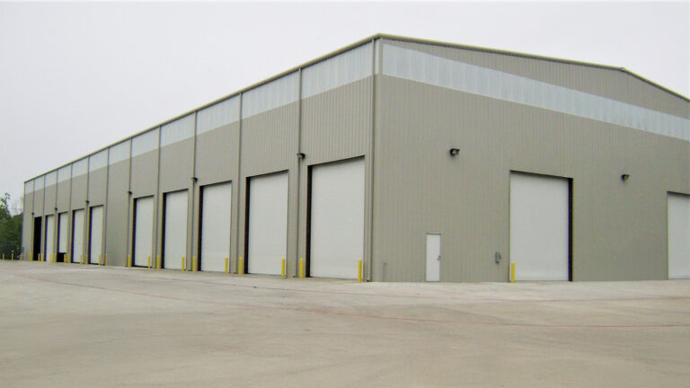 Front exterior of a metal building at Master Rig International in Houston, TX by Keeton Construction Services with multiple overhead doors and a paved apron