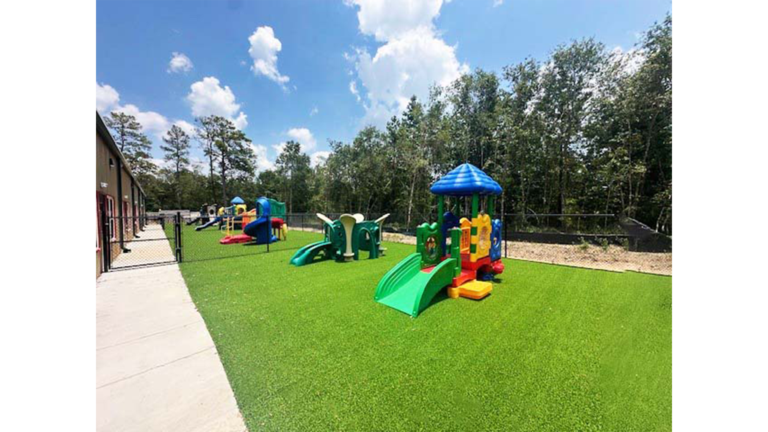 Little Texans Day Care Center outdoor playground area with colorful play equipment on synthetic turf, Conroe, TX - Keeton Construction Services